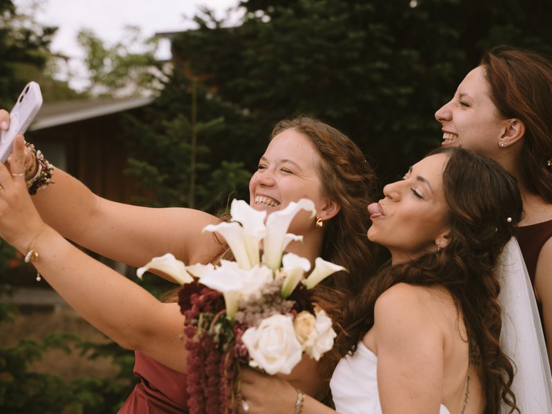 Ani und zwei Freundinnen machen ein fröhliches Selfie mit dem Brautstrauß aus weißen Callas.