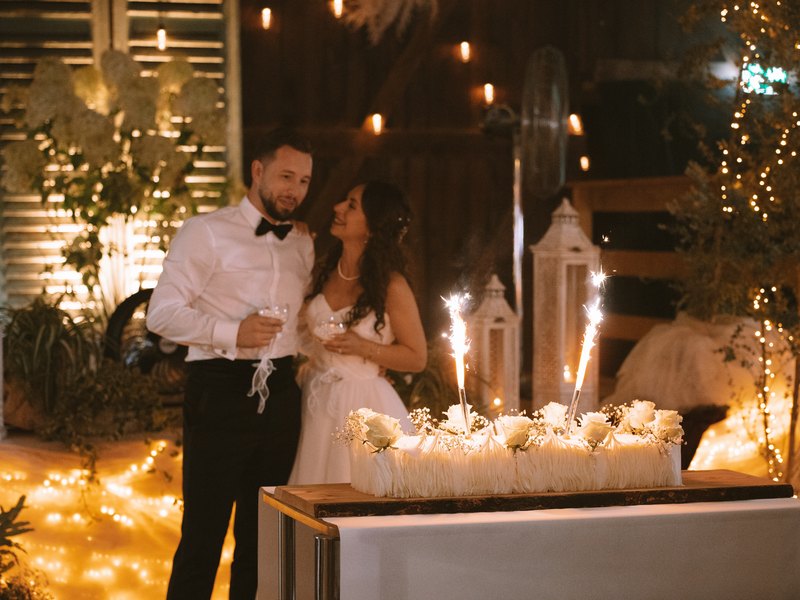 Ani und Elias stehen im warmen Lichterglanz vor ihrer Hochzeitstorte mit Wunderkerzen.